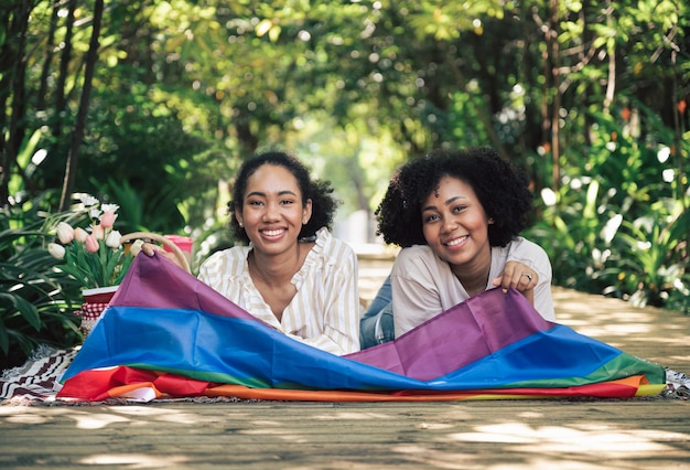 Two young beautiful smiling girls with LGBT flag in the garden