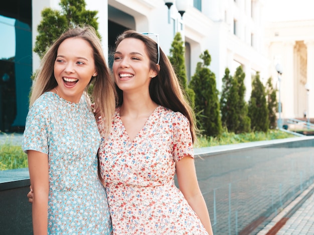 Two young beautiful smiling hipster female in trendy summer dressesSexy carefree women posing in the street Positive pure models having fun at sunset hugging and going crazy