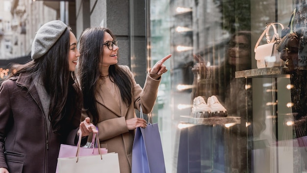 Two young beautiful women enjoy shopping while pointing finger in the shopwindow