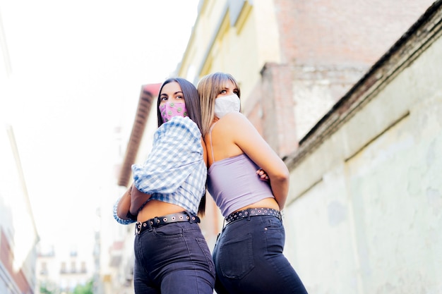 Two young beautiful women meet in the city Covid-19 - Millennial having fun together with facial mask after the lockdown