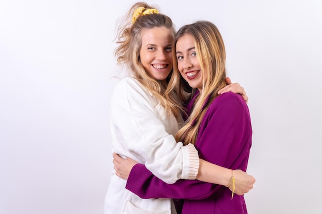 Two young blonde Caucasian women friends hugging and smiling isolated on a white background