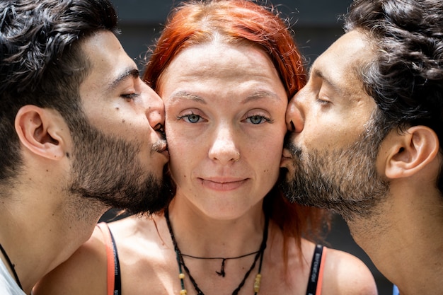 Two young boys of different ethnicities kissing on the cheek of a girl standing in the middle