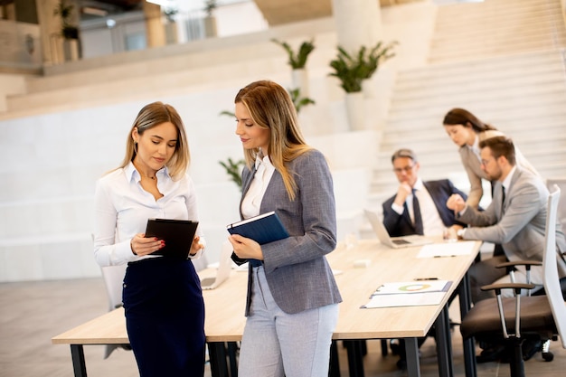 Two young business women looking at financial results on digital tablet in front of their team at the office