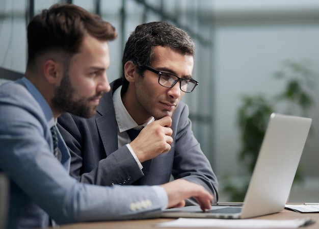 Two young businessmen sitting at workplace and working together in office