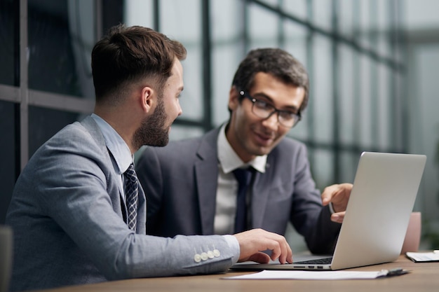 Two young businessmen sitting at workplace and working together in office