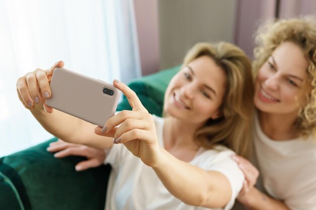 Two young and cheerful girls taking selfie together at home