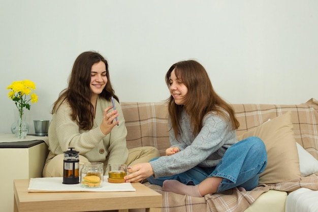 Two young cheerful women drink tea and use a mobile phone communicate on positive topics