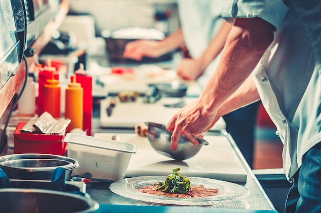 Two young chefs in white uniform preparing delicious fish meat snack salad only hands close up