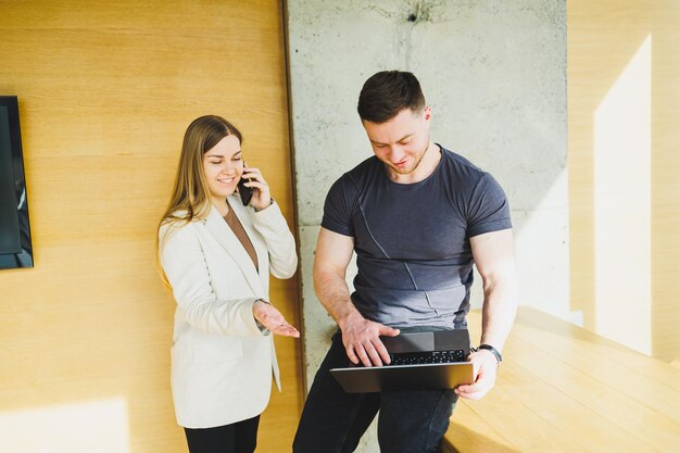 Two young colleagues man and woman working together in a modern workspace Two young businessmen smiling cheerfully while working with a laptop Colleagues sit together at the table