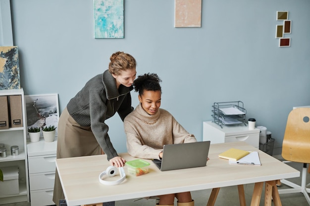 Two young colleagues working over website on laptop together at table at office