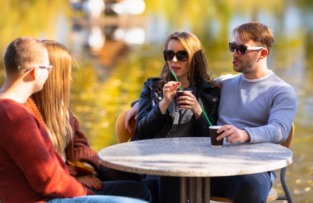 Photo two young couples enjoying coffee outdoors as they sit chatting at an outdoor restaurant overlooking a lake in autumn