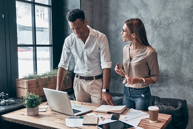 Two young coworkers in smart casual wear discussing business while working in the office