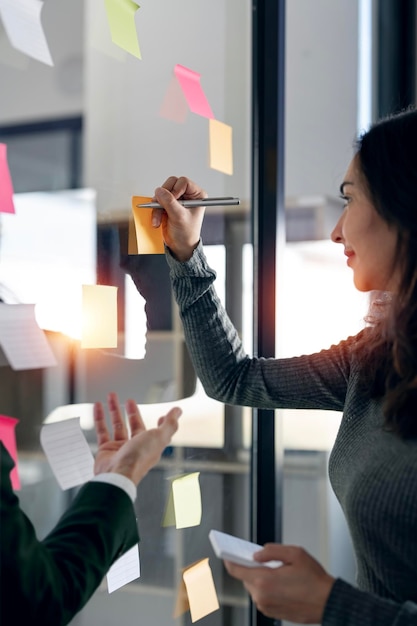 Two young creative team using post it notes in glass wall to writing strategy and business plan