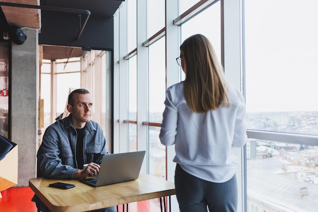 Two young entrepreneurs behind a laptop watch a presentation in the office and discuss the company's development plan. Young manager tells subordinate woman to manager how to keep notes in laptop