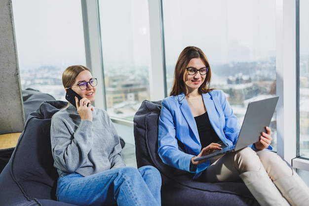 Two young female freelancers working remotely in the lounge area at a laptop The concept of remote work Friendly relations between colleagues