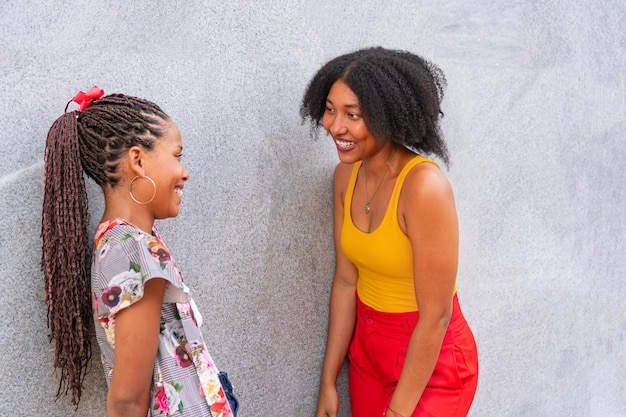 Two young friends talking in the sunlight on the city street on a gray wall