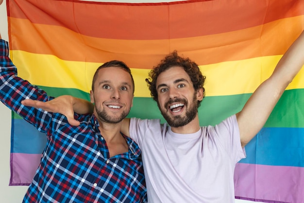 Two young gay lovers looking at each other affectionately Two young male lovers standing together against a pride flag Affectionate young gay couple sharing a romantic moment together