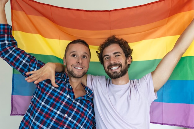 Two young gay lovers looking at each other affectionately Two young male lovers standing together against a pride flag Affectionate young gay couple sharing a romantic moment together