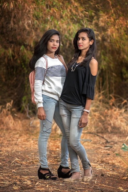 Two young girl friends standing together and having fun in outdoors. Looking at camera.