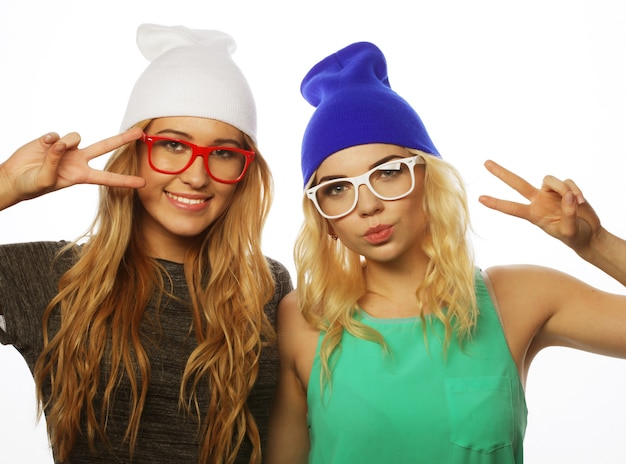 Two young girl friends standing together and having fun. Showing signs with hands. Looking at camera