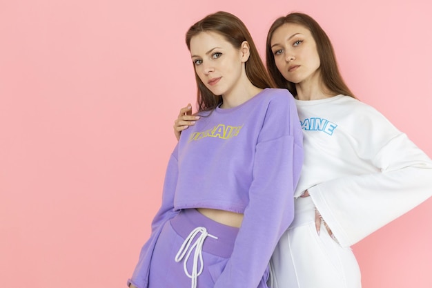 Two young girls in tracksuits pose against a pink background