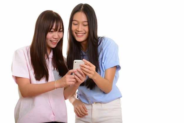 Two young happy Asian teenage girls smiling and using mobile phone