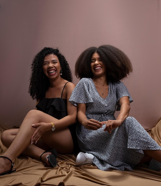 Two young happy beautiful friends looking at the camera sitting against a salmoncolored background