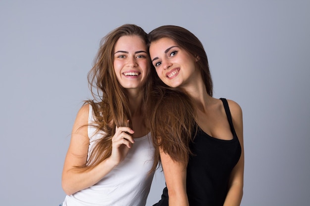 Two young happy women in black and white shirts embracing on gray background in studio