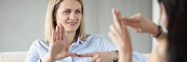 Two young happy women sitting on couch and making sign languages deaf and dumb communication