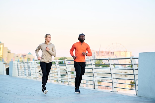 Two young intercultural athletes in sport jackets leggins and sneakers