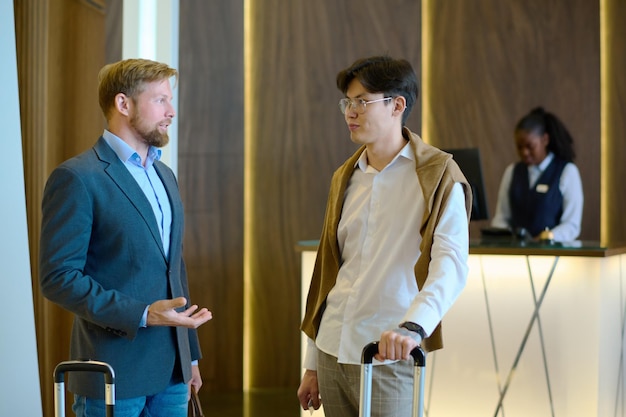 Photo two young intercultural businessmen with suitcase having discussion in lounge