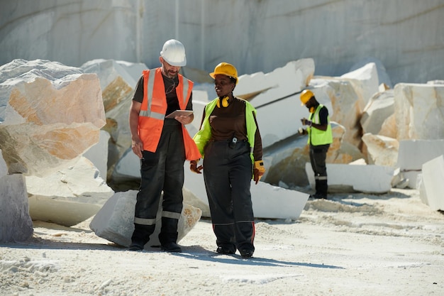 Two young intercultural workers of marble quarry discussing online manual guide