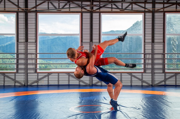 Two young men in blue and red wrestling tights are wrestlng and making a suplex wrestling 