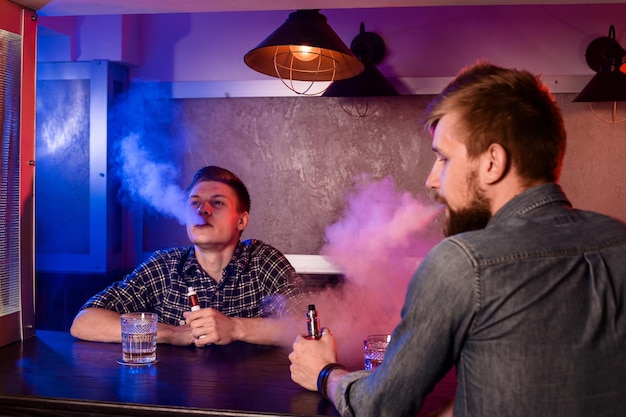 Two young men smoke electronic cigarettes in a vapebar. Vape shop