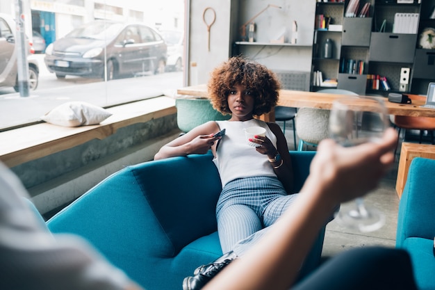 Two young multiracial women sitting in modern pub and drinking together