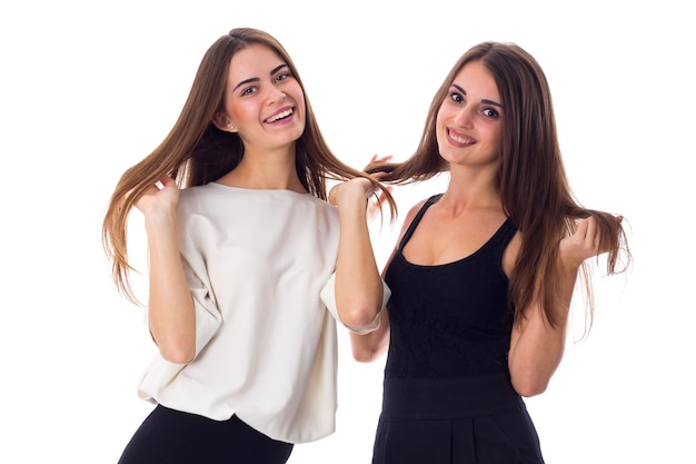 Two young pretty women in black and white shirts touching hair on white background in studio