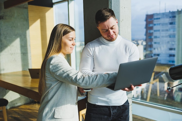 Two young promising colleagues man and woman are talking and working on a new project at a laptop Work in a bright modern office Team work