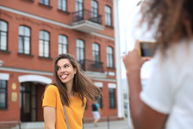 Two young smiling hipster women in summer clothes posing on street.Female showing positive face emotions.