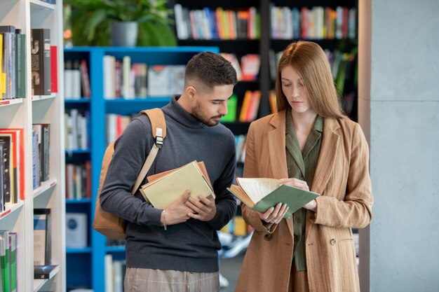 Two young students choosing books in library or bookshop