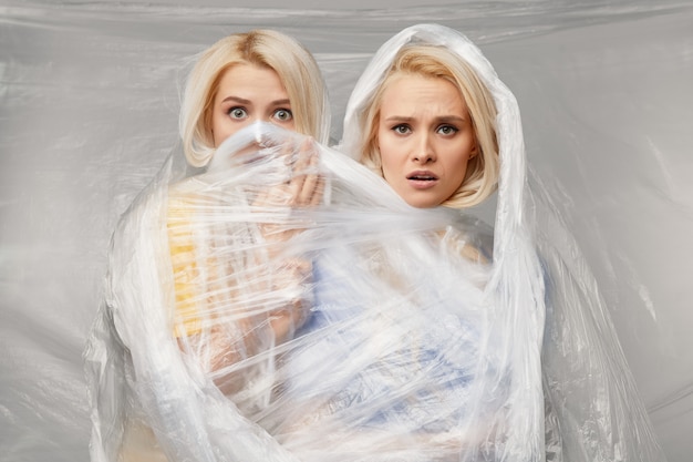 Two Young upset women wrapped in indestructible polyethylene. The problem of environmental pollution and poor ecology. Volunteers