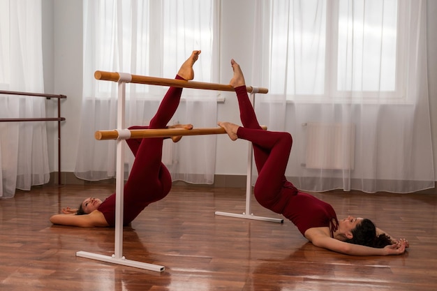 Two young womans fitness instructor in red sportswear leggings and top stretching in the gym before