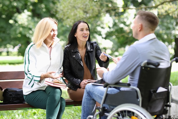 Two young women communicate with a man in wheelchair in park support with people with