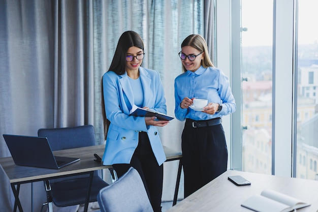 Two young women managers work in a modern office Women colleagues are talking while working Friendly staff