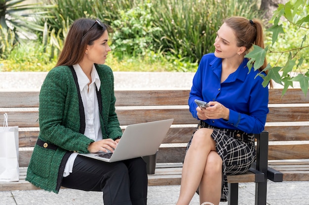 Two young women sitting on a street bench working on their laptop pointing at the screen