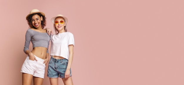 Two Young Women Smiling In Summer Attire Against Pink Background