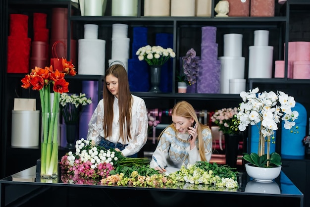 Two young women take orders by phone and make beautiful festive bouquets in a cozy flower shop Flori