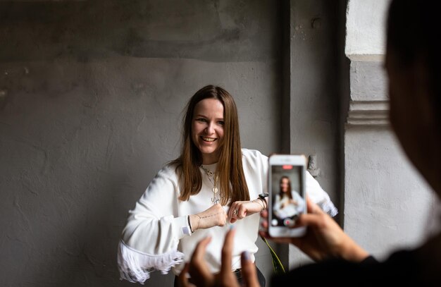 Two young women take photos and videos of each other on smartphone on a terrace