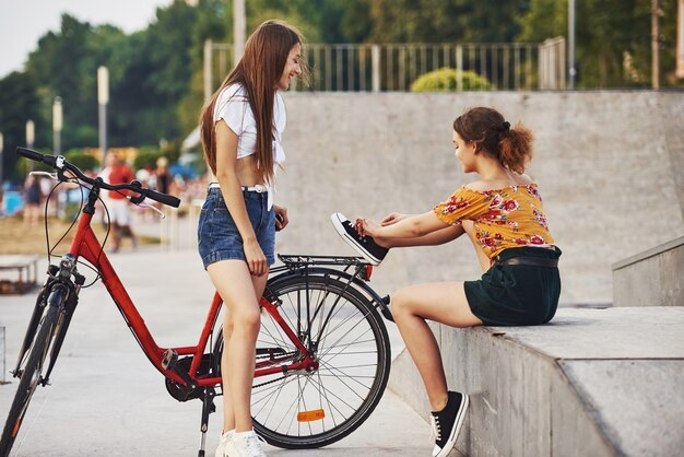 Two young women with bike have a good time in the park near the ramp.