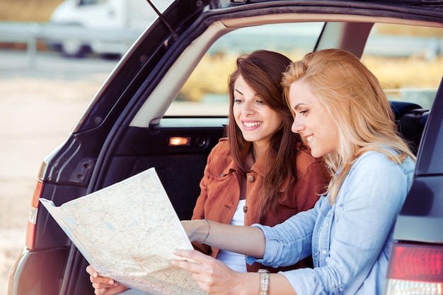 Two young women with car look at road map