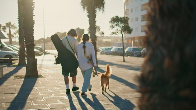 Two youngsters walking summer street with pet back view guy embracing woman